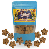 A blue stand-up pouch of dog treats with a clear window showing brown flower-shaped treats inside, surrounded by several loose flower-shaped treats on a white background. The front label reads 'PUT YOUR PAWS UP AND CHILL' with an illustration of a dog on a couch.