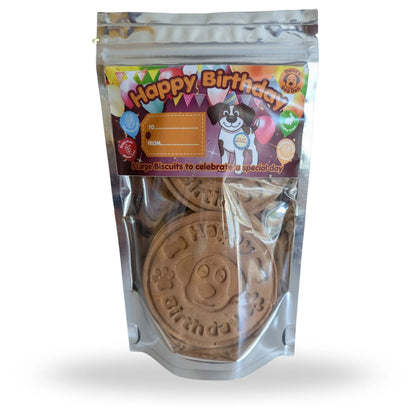 A stand-up resealable pouch of dog birthday biscuits. The clear plastic bag shows round brown biscuits stamped with 'Happy Birthday' and paw prints.