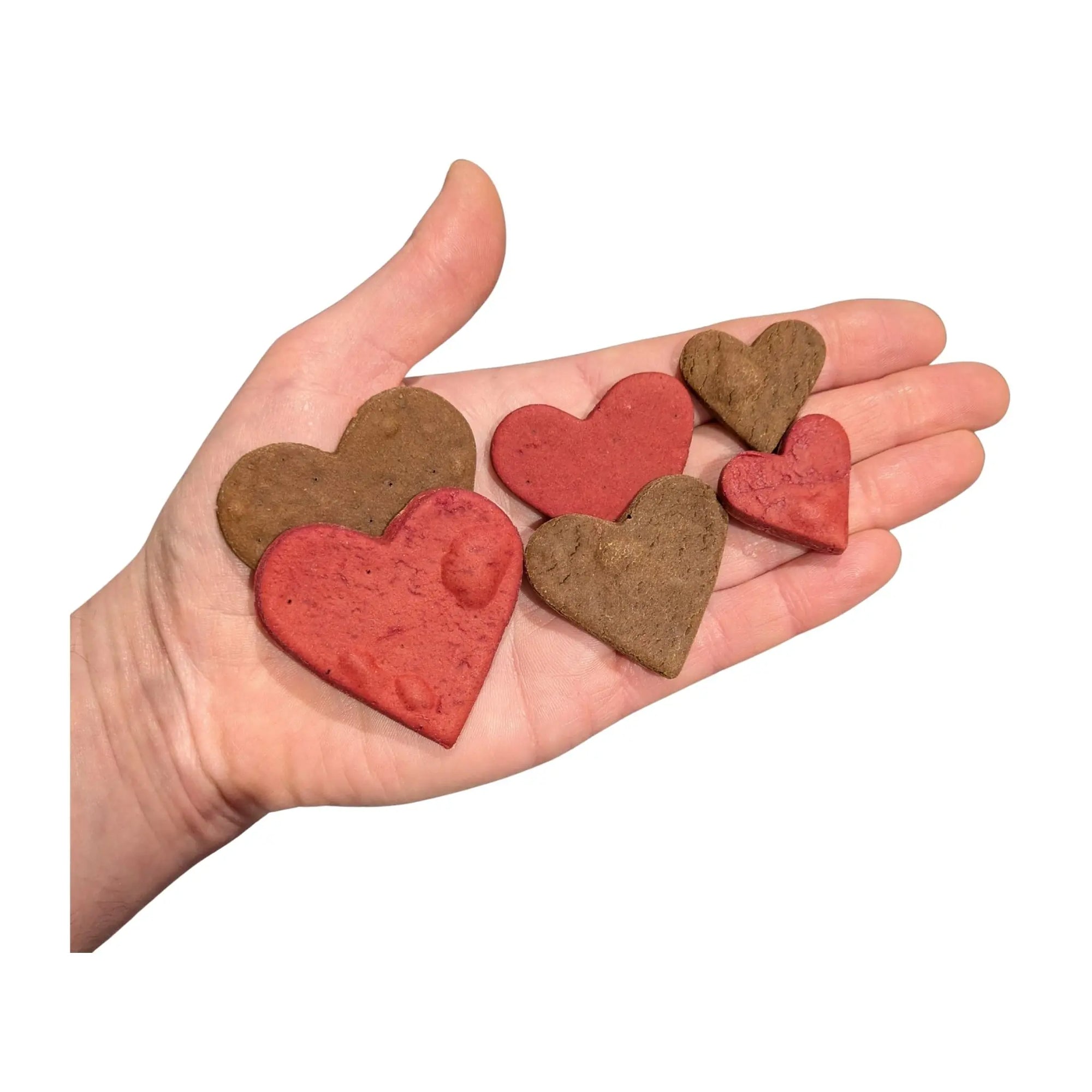 Hand holding heart-shaped beetroot and carob dog treats 