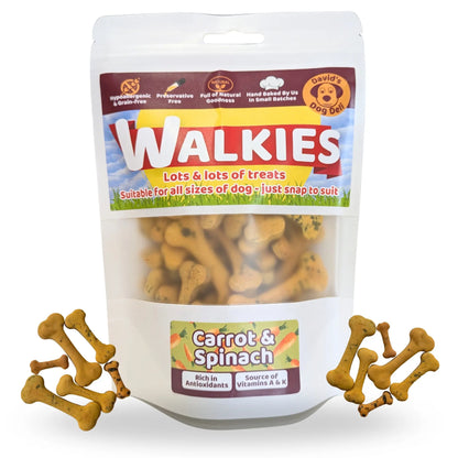 A stand-up pouch of Walkies dog treats, labeled 'Carrot & Spinach,' with several bone-shaped treats scattered around the base on a white background.